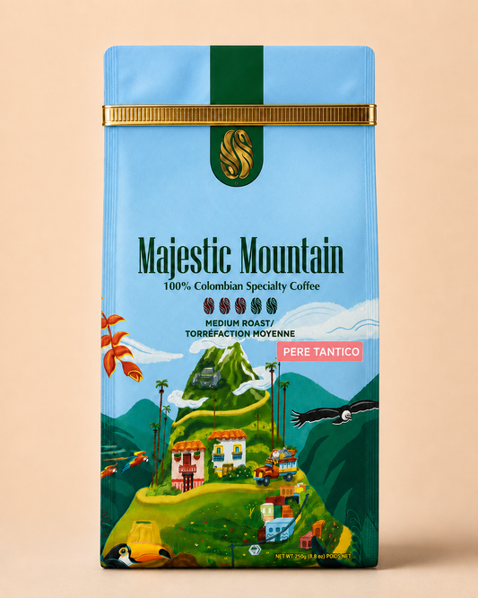 A package of Majestic Mountain Colombian Specialty Coffee, featuring a light blue and green illustrated design with a gold band at the top, set against a solid beige background.