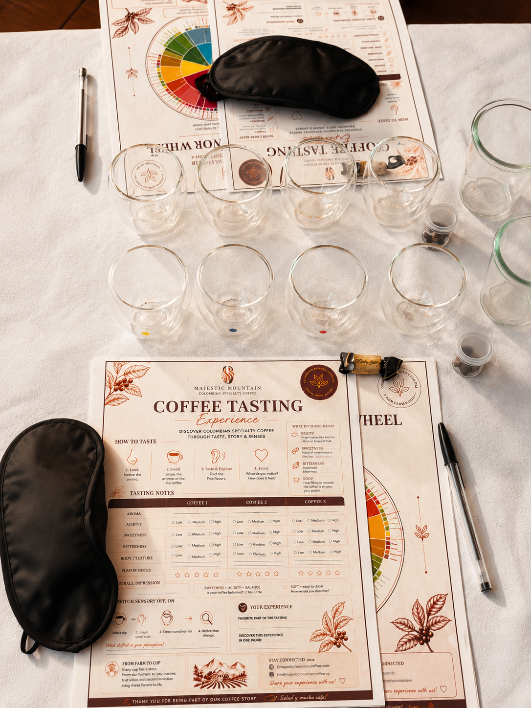 Coffee tasting setup with glasses, menu, and sleep masks on a white tablecloth.
