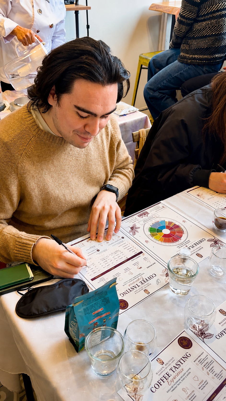 Man sitting at a table with a coffee tasting menu, surrounded by glasses and a tablet.